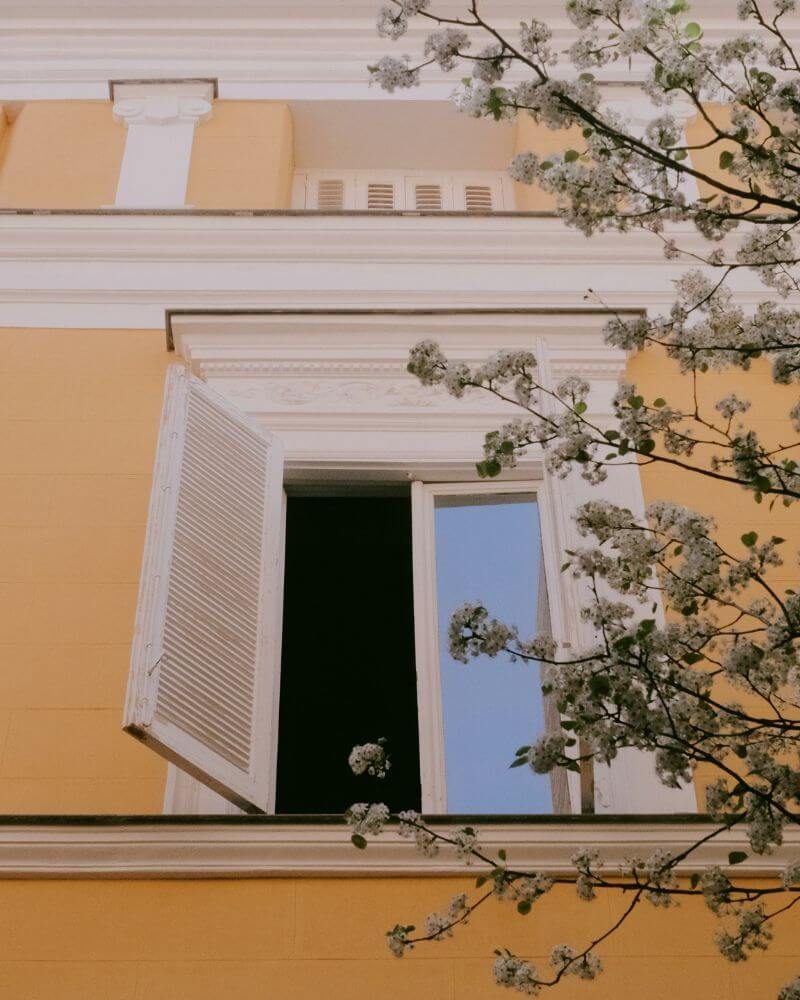 An open shuttered window on a warm yellow Madrid facade, spring blossom in front